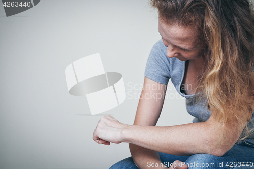 Image of one sad woman sitting near a wall