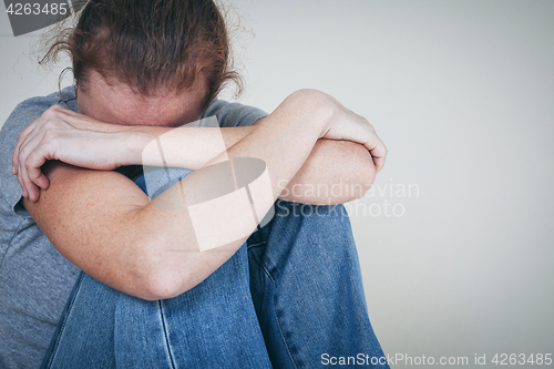 Image of one sad woman sitting near a wall