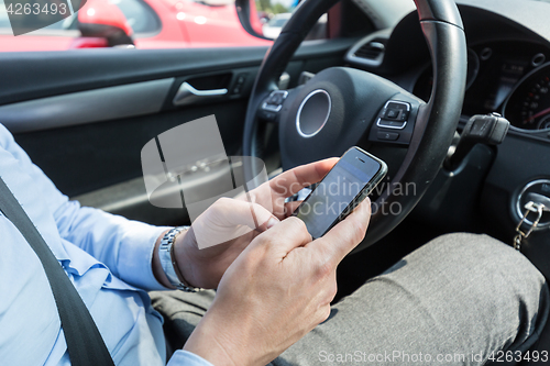 Image of Businessman texting on his mobile phone while driving.