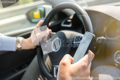 Image of Businessman texting on his mobile phone while driving.