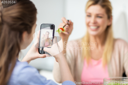 Image of girl photographing mother by smartphone at home