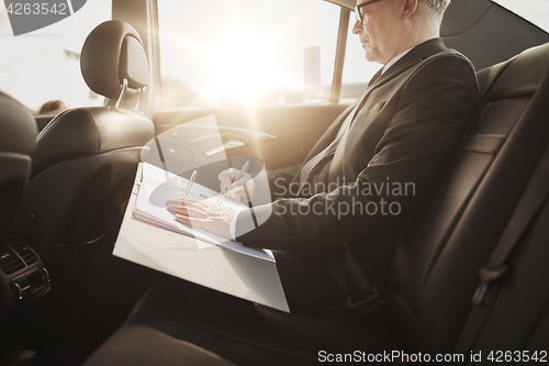 Image of senior businessman with papers driving in car