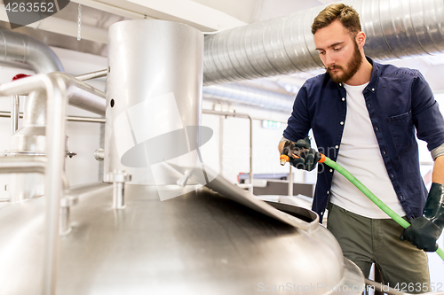 Image of man with hose working at craft beer brewery kettle