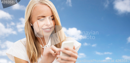 Image of happy woman with smartphone and earphones over sky