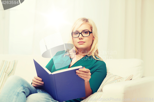 Image of young woman in glasses reading book at home