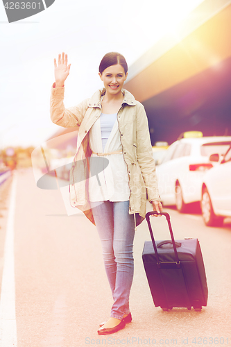 Image of smiling young woman with travel bag over taxi