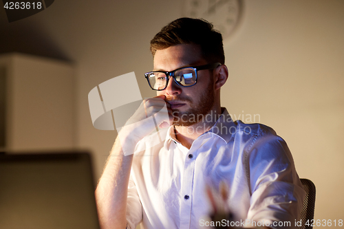 Image of businessman in glasses with laptop at night office