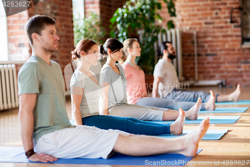Image of group of people doing yoga staff pose at studio