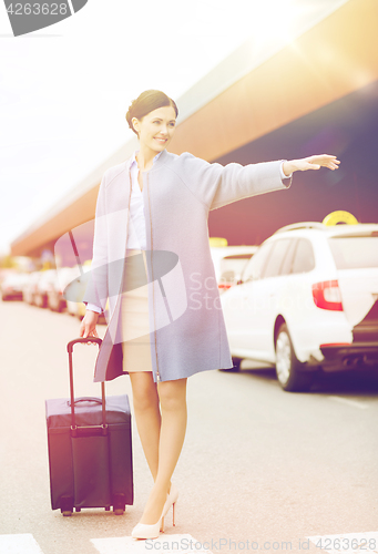 Image of smiling young woman with travel bag catching taxi