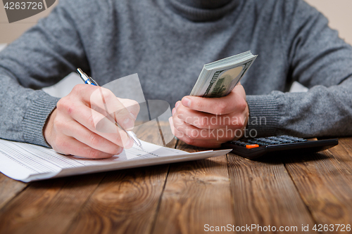 Image of Caucasian hands counting dollar banknotes on dark wooden table