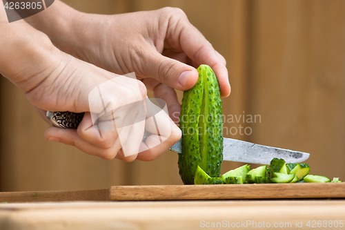 Image of hands cutting cucumber on the wooden cutting board