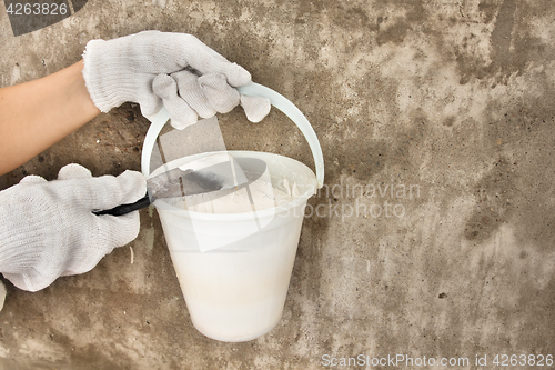 Image of hands holding bucket with plaster and spatula