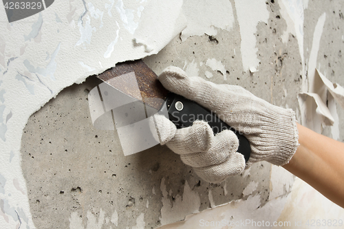 Image of hand removing wallpaper from wall with spatula