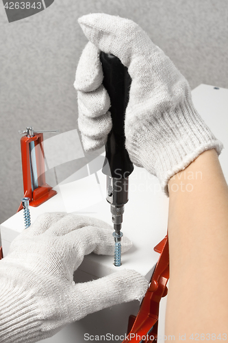 Image of hands assembling furniture from chipboard with screwdriver