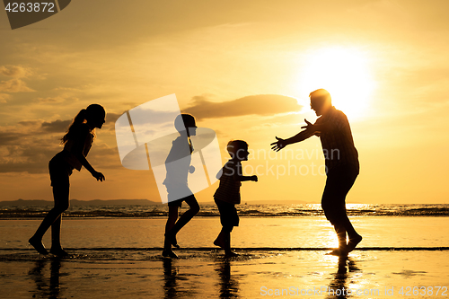 Image of Father and children playing on the beach at the sunset time.