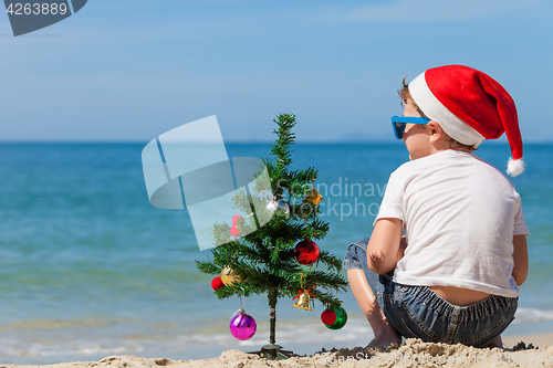 Image of Happy little boy sitting on the beach at the day time. 