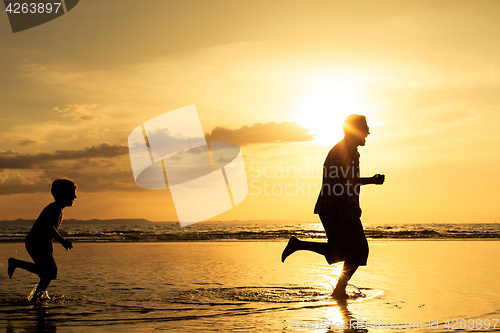 Image of Father and son playing on the beach at the sunset time.