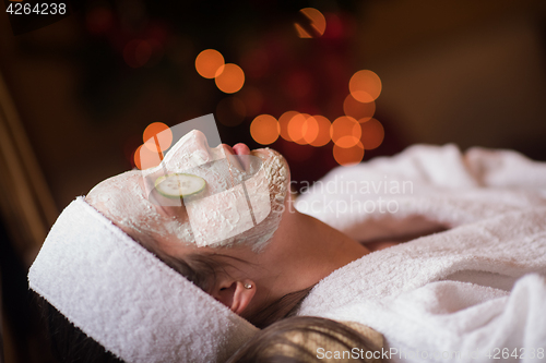 Image of woman is getting facial clay mask at spa