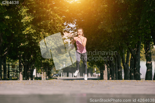 Image of Pretty sporty woman jogging at park in sunrise light