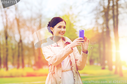 Image of smiling woman taking picture with smartphone