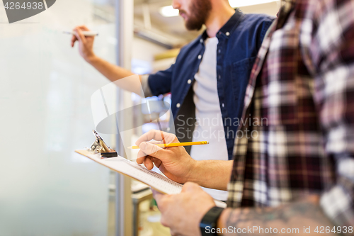 Image of men writing to clipboard and whiteboard at office