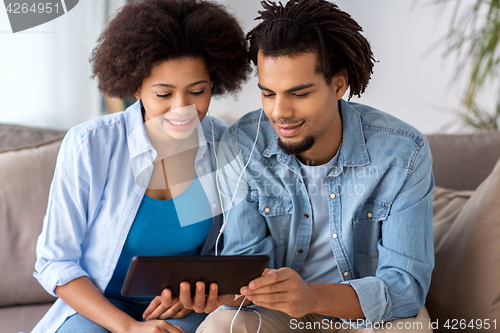 Image of happy couple with tablet pc and earphones at home