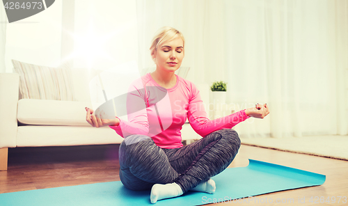 Image of happy woman stretching leg on mat at home