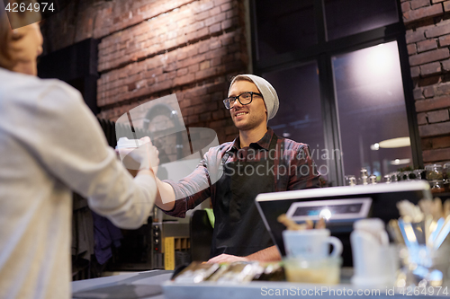 Image of seller giving coffee cup to woman customer at cafe