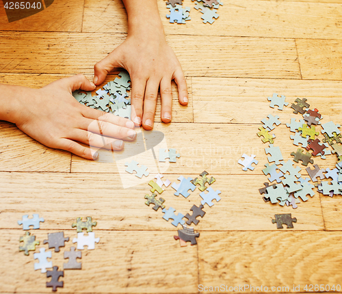 Image of little kid playing with puzzles on wooden floor together with pa