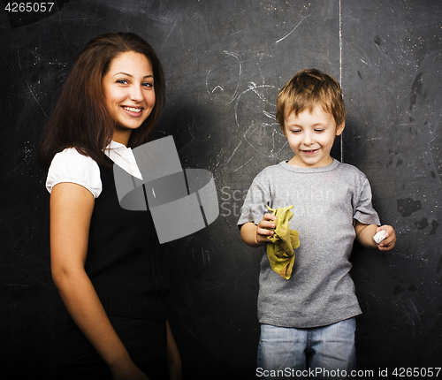 Image of little cute boy with young teacher in classroom studying at blac