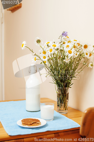 Image of Simply stylish wooden kitchen with bottle of milk and glass on table, summer flowers camomile, healthy foog moring concept