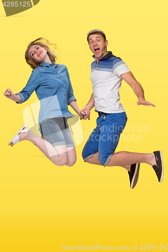 Image of Portrait of a young couple jumping against yellow background