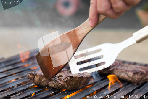 Image of Chef grilling beef steaks on open flame BBQ.