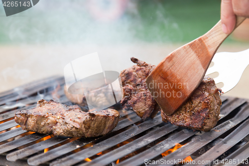 Image of Chef grilling beef steaks on open flame BBQ.