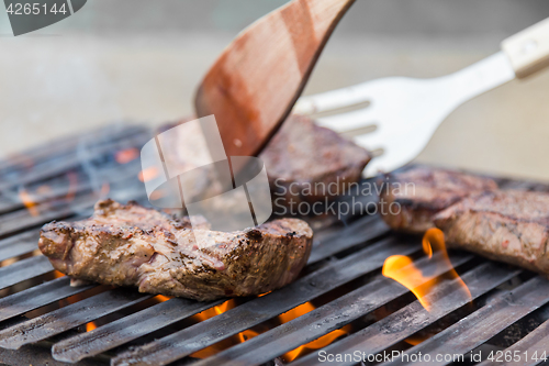 Image of Chef grilling beef steaks on open flame BBQ.