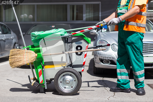 Image of Worker of cleaning company in green uniform with garbage bin.