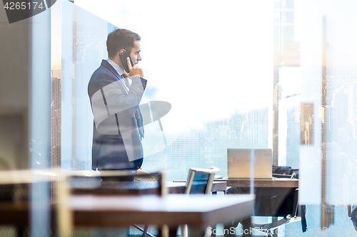 Image of Businessman talking on a mobile phone while looking through window in NY