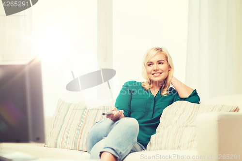 Image of smiling woman with remote watching tv at home