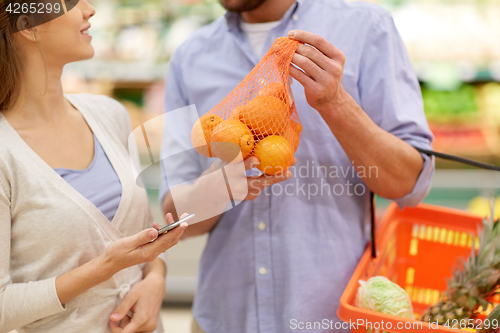 Image of couple with smartphone buying oranges at grocery