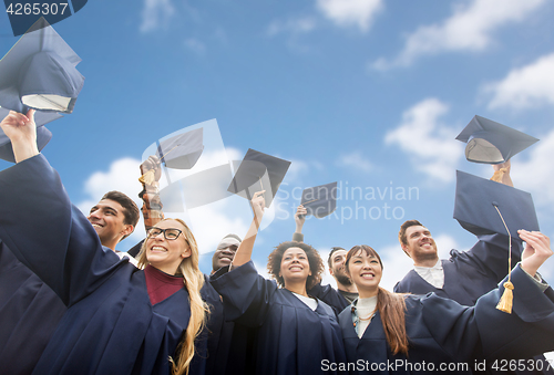 Image of happy bachelors waving mortar boards over sky