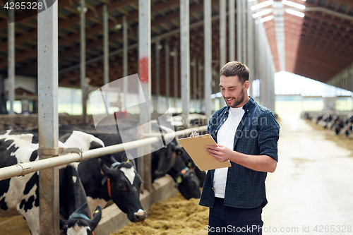 Image of farmer with clipboard and cows in cowshed on farm