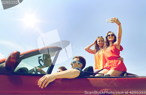 Image of friends driving in cabriolet car and taking selfie