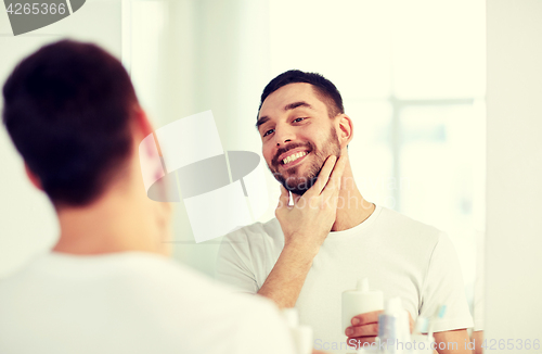 Image of happy man applying aftershave at bathroom mirror