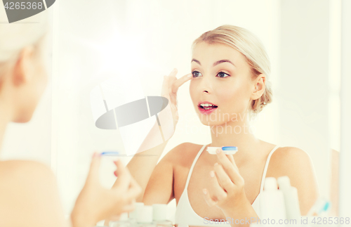 Image of young woman putting on contact lenses at bathroom