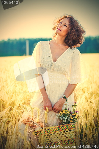 Image of beautiful smiling woman in a white dress standing among the ears