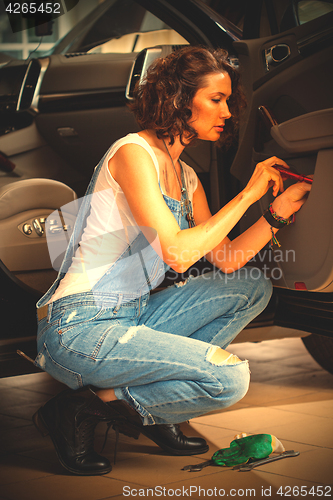 Image of Woman car mechanic in blue overalls adjusts the car door