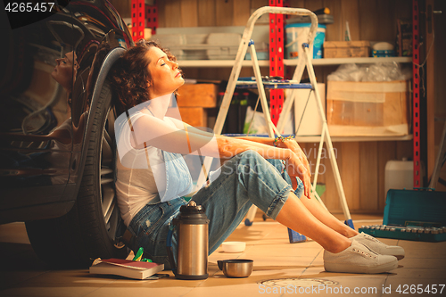 Image of woman a car mechanic sits in a blue overall in a garage near a c
