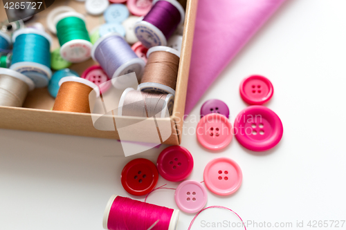 Image of box with thread spools and sewing buttons on table