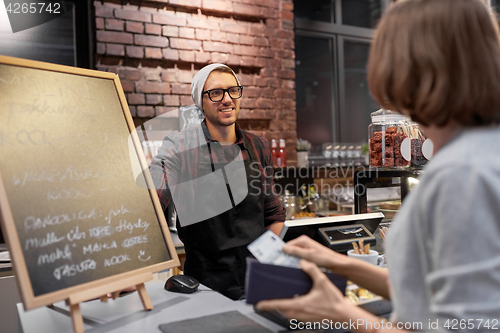 Image of happy barman and woman paying money at cafe