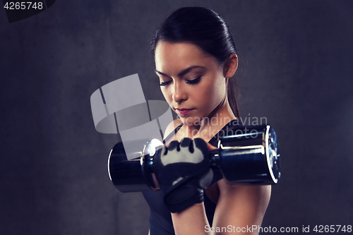 Image of young woman flexing muscles with dumbbells in gym